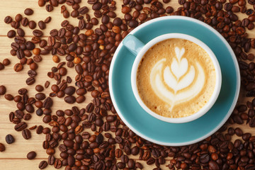 A cup of fragrant coffee in foam on a wooden table. Latte art. Coffee beans.