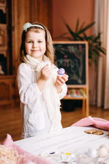 Smile girl colours eggs for Easter at home.  Easter objects, things, laying on white wooden table, daughter's hands painting, decorate eggs, holding brushed