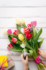 Multicolored eggs and tulips with a gift for Easter on a white background. View from above and copy space