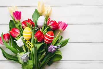 Multicolored eggs and tulips with a gift for Easter on a white background. View from above and copy space