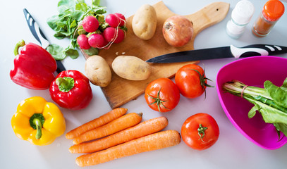 Fresh diverse colorful vegetables being cut and prepared to be cooked on a kitchen counter.