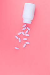 Poured pills and a white can of medicine for a pink pastel background. Flat lay. Top view