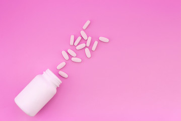 White tablets and a white bottle are isolated on a bright pink background. Medical concept