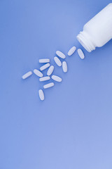 Pills are poured from a white bottle on a pastel blue background. Place for text.Flat lay