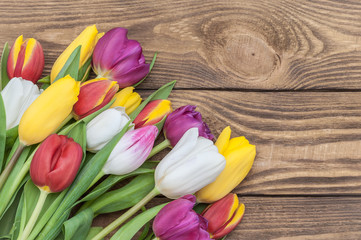 A bunch of multicolored tulips in a corner on a background of light wood.