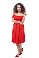 Beautiful curly female in red dress and red high heels shoes in full length touching her hair in thoughts