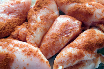 Many raw juicy sliced chicken pieces well sprinkled with red pepper, are ready for baking top view closeup