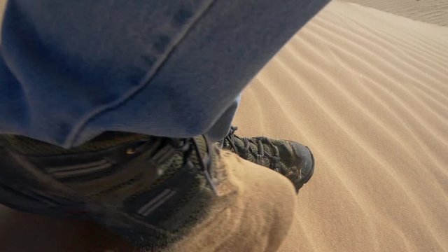 A man's feet hiking on sand dunes in slow motion