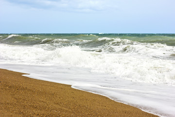 Stormy sea and blue sky, white sea foam on a yellow sandy beach.