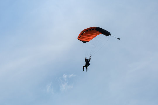 Parachutist with Orange Parachute against Clear Blue Sky