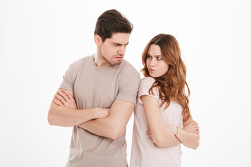 Photo of adult guy and girl wearing beige t-shirts acting like arguing couple and not speaking to each other standing back to back with crossed arms, over white background
