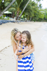 Fototapeta na wymiar Young blonde mother cuddles and is playing with her daughter on the beach and havin fung