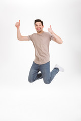 Full-length photo of handsome man 30s in casual t-shirt and jeans jumping and rejoicing with gesturing thumbs up, isolated over white background