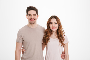 Amazing portrait of young married people 20s man and woman wearing beige t-shirts posing together while smiling and hugging each other, over white background
