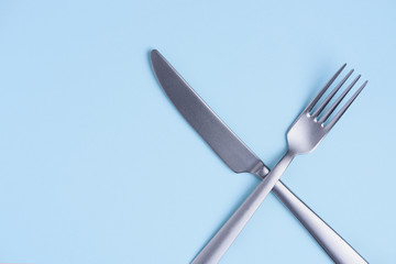 Crossed silver metal knife and fork sign on trendy blue pastel background with side copy space