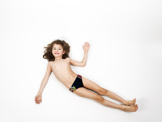 Adorable little boy in a swimsuit lying on the floor, isolated on a light