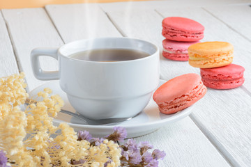 Different types color of macaroons with Cup of hot tea on white wooden background
