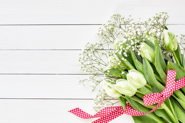 Bouquet of white tulips and gypsophila decorated with red ribbon on white wooden background. Top view, copy space