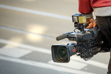 cameraman holding his professional camcorder in the street. Operator in social environment,...