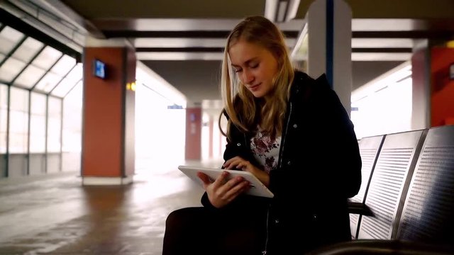 Young, teenager girl sitting with tablet at the train station
