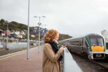 Young woman standing on railway platform using her mobile phone