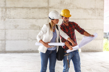 Female inspector and architect discuss with head engineer about blueprints on construction site.