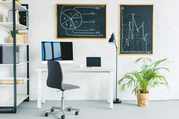 Computers on table in light office with business charts on walls