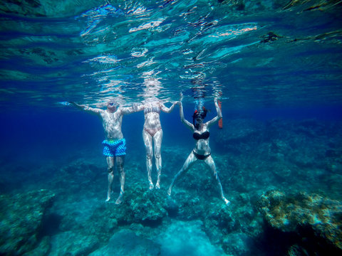 Underwater photo of three young playful adventuristic handsome student friends diving and swimming with goggles and snorkelling mask in the exotic turquoise sea at summer vacation.