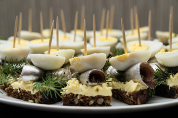 Mini sandwich with salt sprat and sliced boiled quail egg on the slice of bread. Canned fish is...