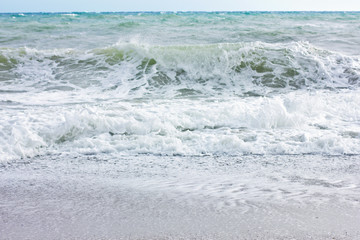 Stormy sea and blue sky, white sea foam on a yellow sandy beach.