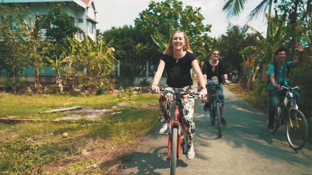 Cute young blonde woman waves to someone while riding a bike through Ho Chi Minh City with her friends
