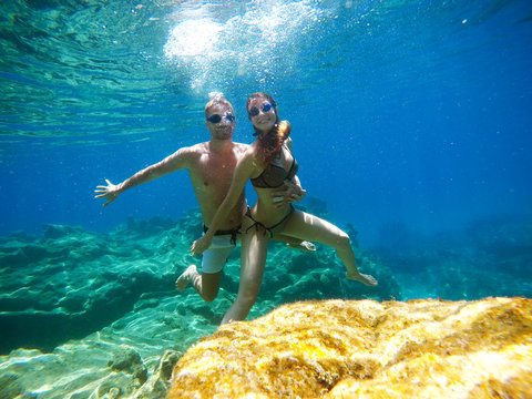 Underwater photo of young attractive playful love couple exploring and enjoying with goggles in the exotic turquoise sea near the coral reef while diving together.