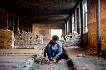 Close up view of sporty active afro american runner man crouching and tying velcro sneakers in the abandon place.