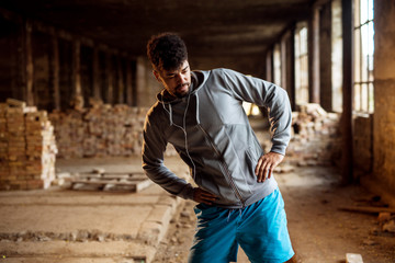 Obraz premium Close up portrait of active afro-american young attractive athletic man doing stretching workout inside of the abandoned place.