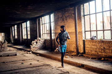 Obraz na płótnie Canvas Portrait of active motivated afro-american young attractive athletic man with earphones running inside of the abandoned place.