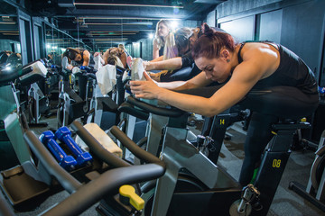 Group of young women in sportswear stretching their legs on exercise bikes before cycling class in gym