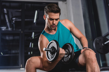 Fototapeta na wymiar strong muscular sportsman lifting dumbbell in gym