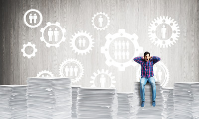 Attractive man sitting on pile of paper documents.