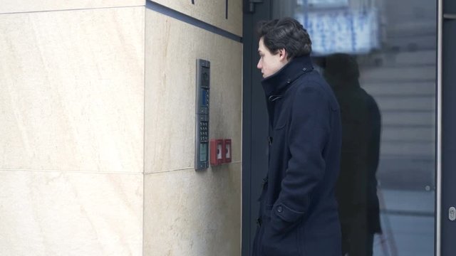 Young teenager talking on intercom by apartment building entrance
