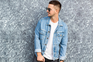 fashion guy standing by a blue marble wall posing in sunglasses