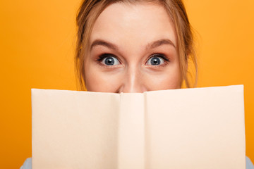 Shocked young lady student covering face with book. Looking camera.