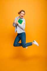 Happy young lady student jumping showing thumbs up.