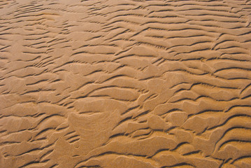 The wet sandy surface is wavy because of the waves.