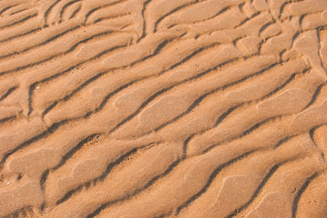 The wet sandy surface is wavy because of the waves.