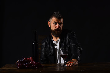 Degustator with strict face sits by wine bottle and grapes