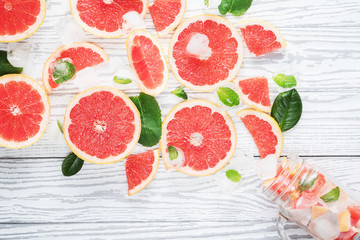 Detox water with grapefruit, mint and ice in mason jar on white wooden table. Summer refreshing drink, pink cocktail, and ingredients with copy space, top view, flat lay. Healthy lifestyle concept.