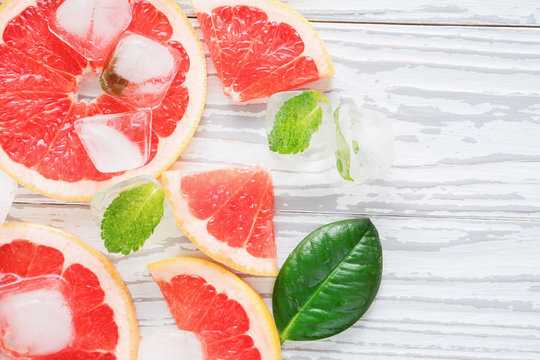 Top view of red grapefruit slices, ice and mint on a white wooden background. The concept of a healthy diet. Detox.