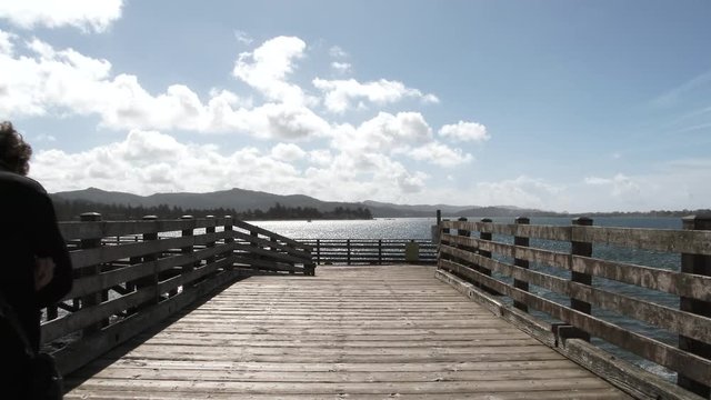 Unrecognizable woman walks down old wooden pier on beautiful day at the Oregon Coast in Lincoln City by the Siletz River and Pacific Ocean.