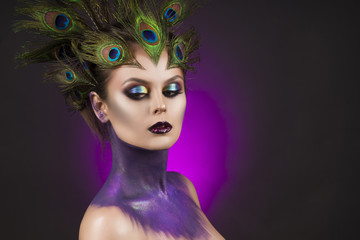 Beautiful big breast girl wearing peacock feathers in her hair and artistic violet shiny body art on her neck, vanguard makeup