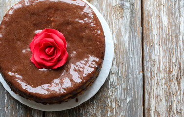 Handmade sponge cake with chocolate frosting. Small cake with cacao ganache glaze. Red sugar rose decorated. Homt pastry. Sweet dessert. Cute birthday cake present.